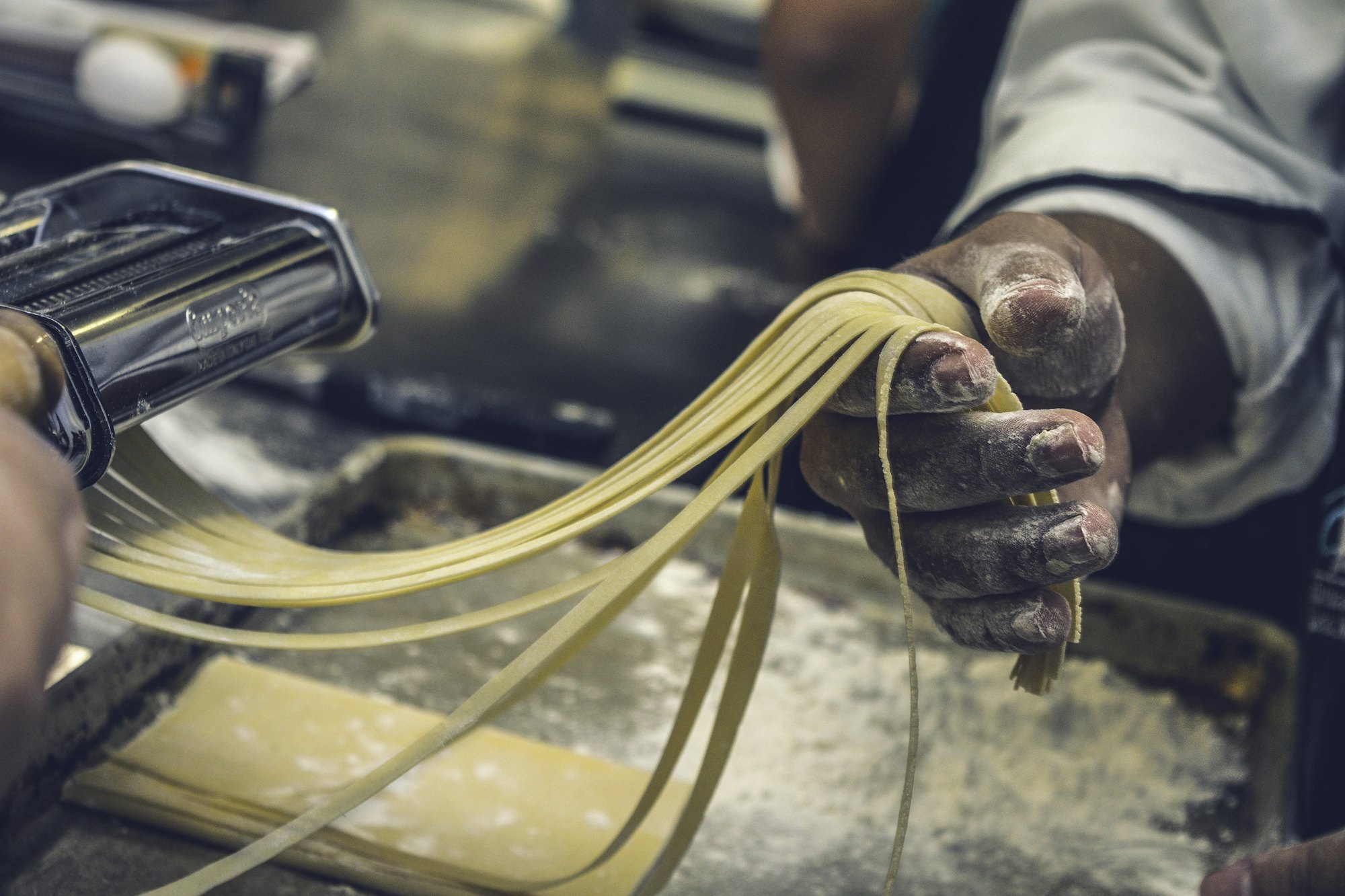 Hands lifting fresh pasta ribbons from a pasta machine